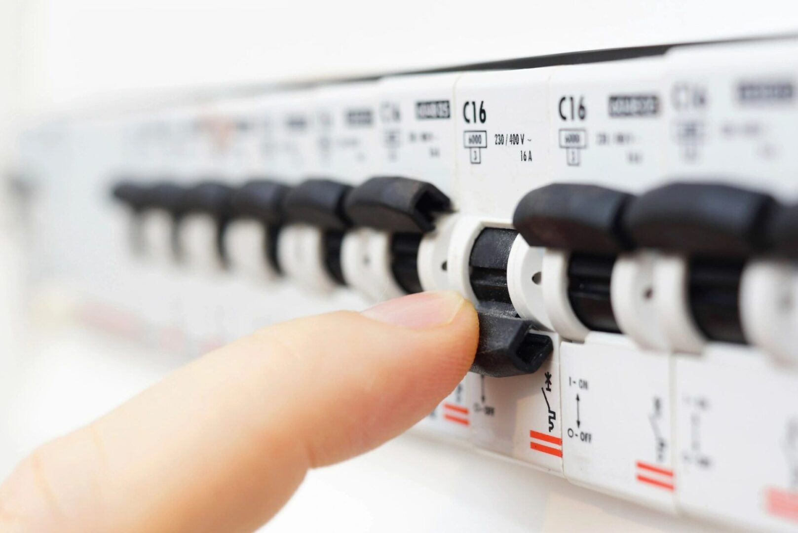 A hand is pressing the button on an electrical panel.